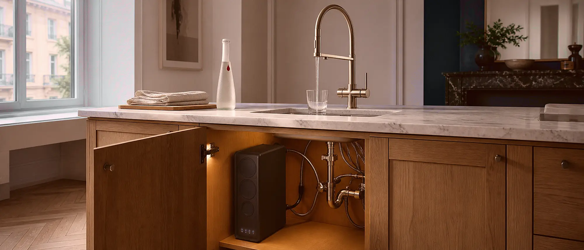 Le meuble entrouvert sous l'évier laisse voir la machine ANNA installée avec soin, pendant que le robinet dédié sert un verre
