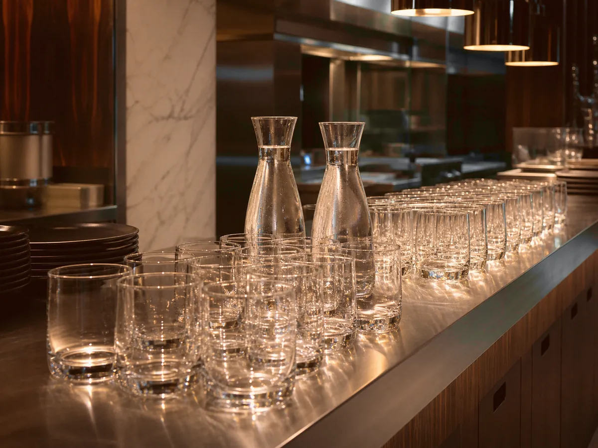 Au passe d'une cuisine professionnelle, des rangées de verres impeccables et deux carafes prêtes